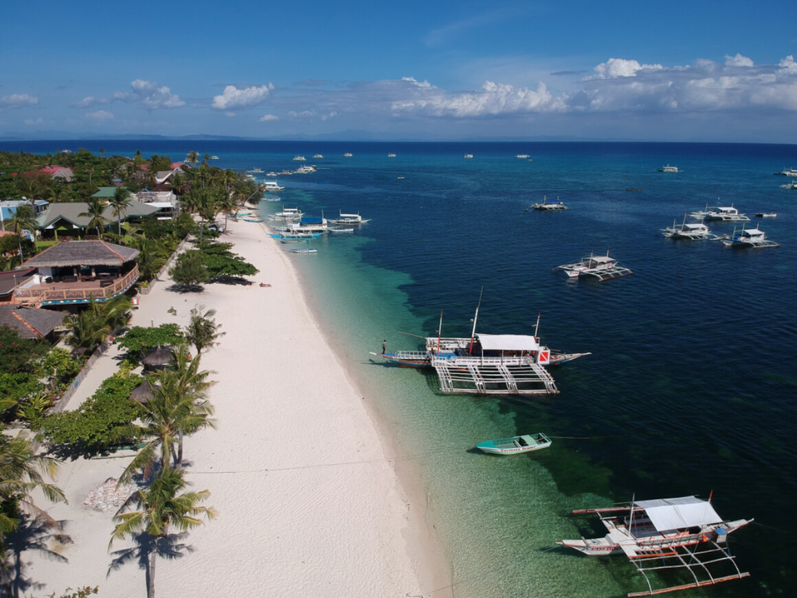 An aerial view of Bounty Beach's coastline with turquoise water, palm trees and boats sailing near the shore.