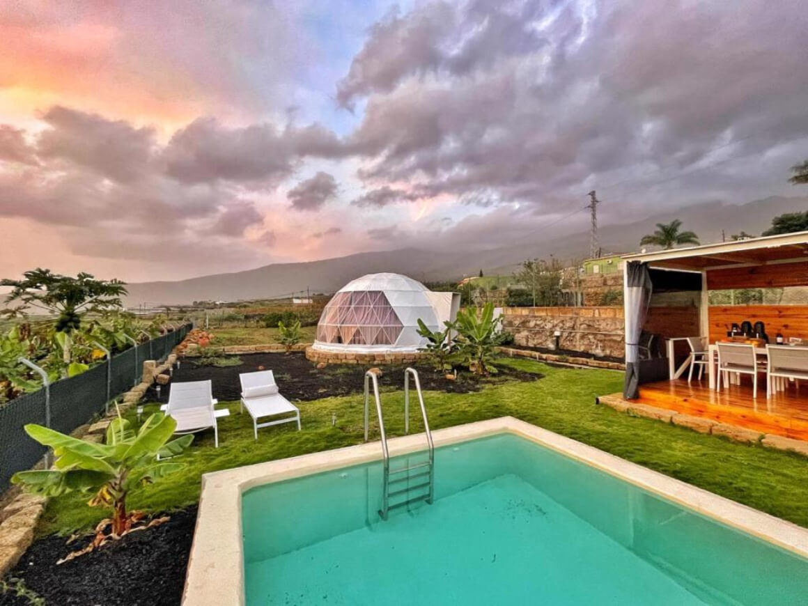 Pool, outdoor dining space and dome accomodation on large grassy land. View of mountains in the distance