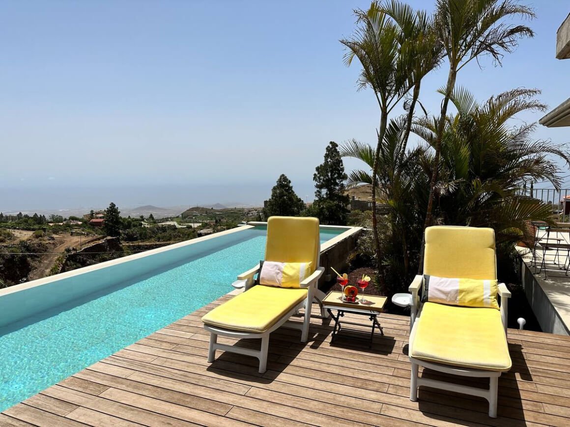 Outdoor area with infinity pool and views of the city. Two yellow sun loungers set up on the deck