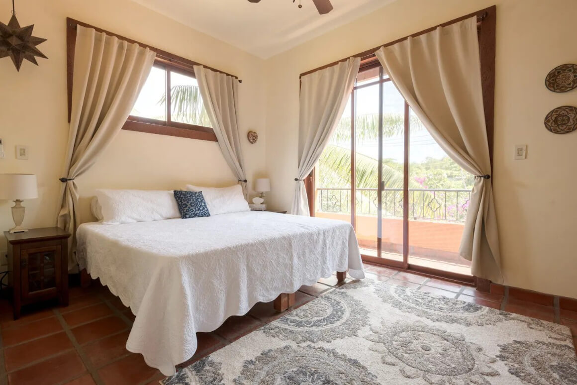 A spacious bedroom with a king-size bed and a sliding glass doors with a balcony. 