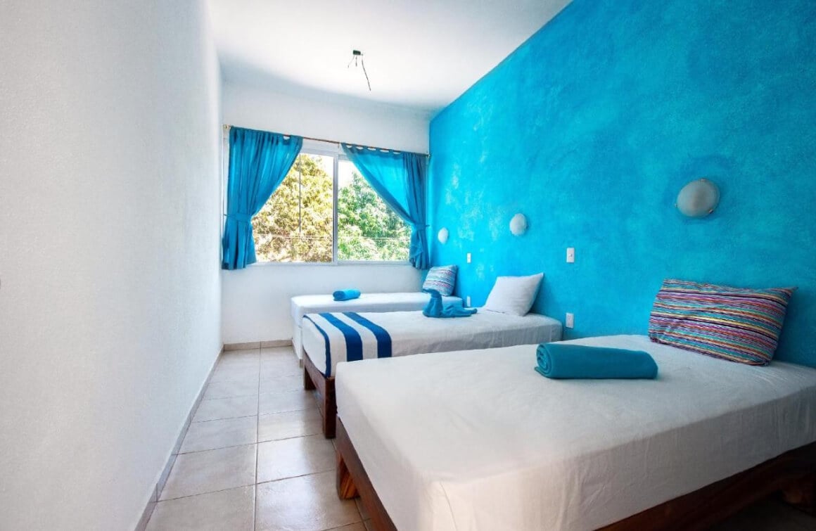 a tripple room at ITH Amazing Hostel Sayulita with a wide window and a blue wall