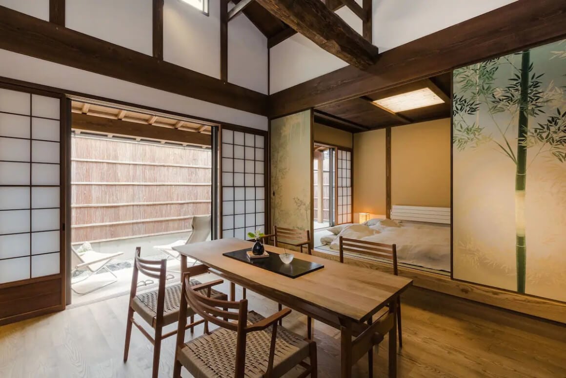 A traditional Japanese room with a dining table, sliding paper doors and a view of a garden in Machiya Ryokan 
