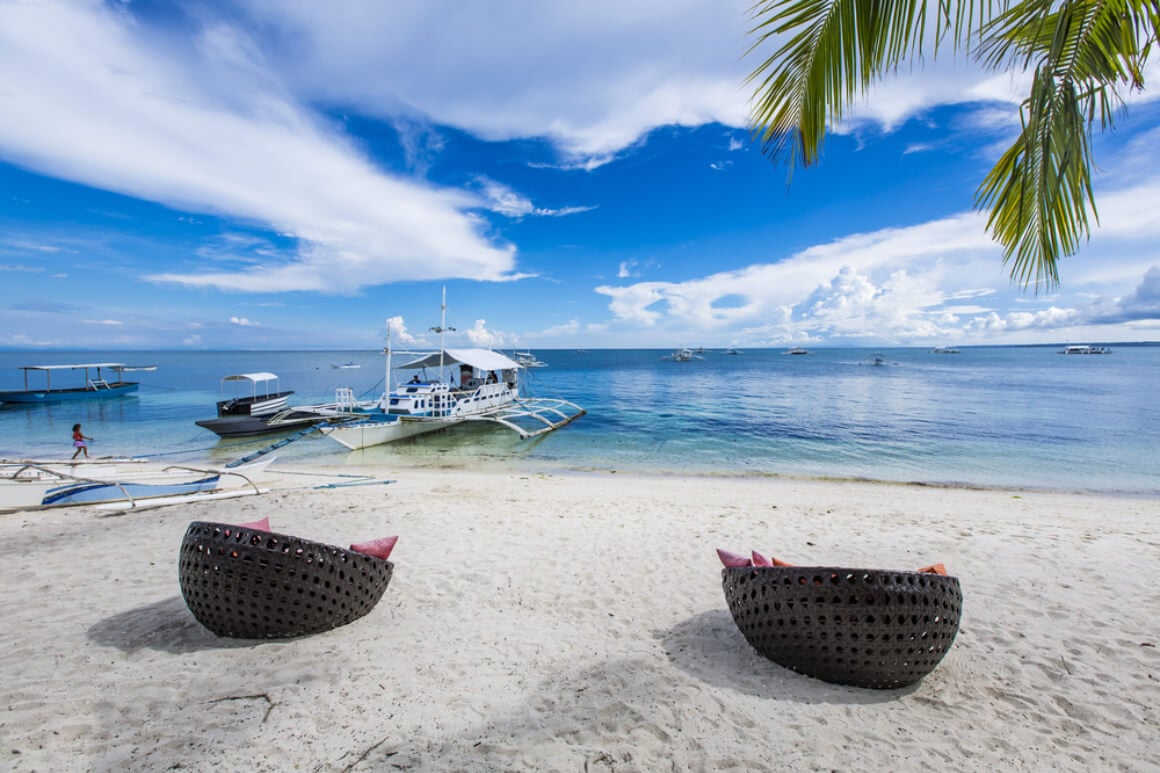 two wicker beach chairs on Logon beach with boasts anchored  by the shoreline