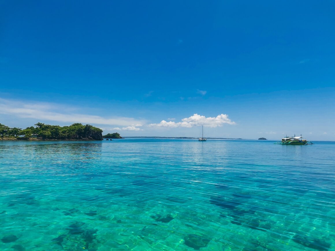 boats floating on a calm, clear, blue ocean in Logon beach,  Malapascua, Philippines