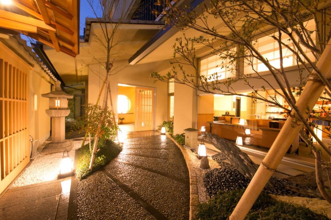 A stone walkway leading to a Ryokan (Matsui Honkan) with a wooden facade and tile roof. 