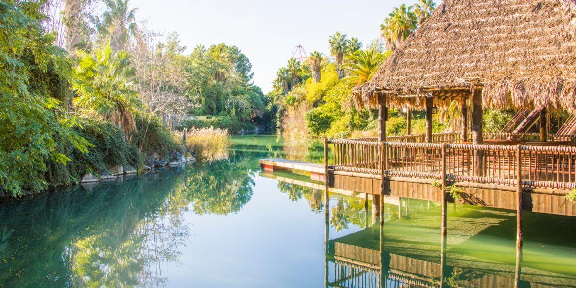 Moorea Tropical Garden with a hut that  extends out into a clear river and surrounded by trees and mountains in the distance. 