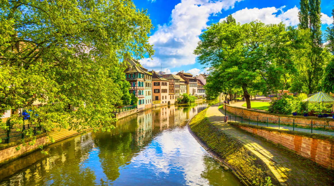 a river surrounded by river by lush greenery and buildings in Neustadt Strasbourg France