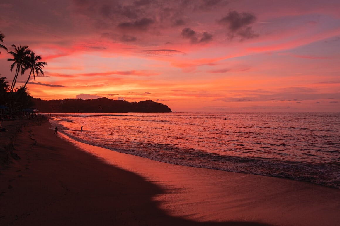 a calm beach in Sayulita Mexico during sunset with golden and pink skies and people swimming 