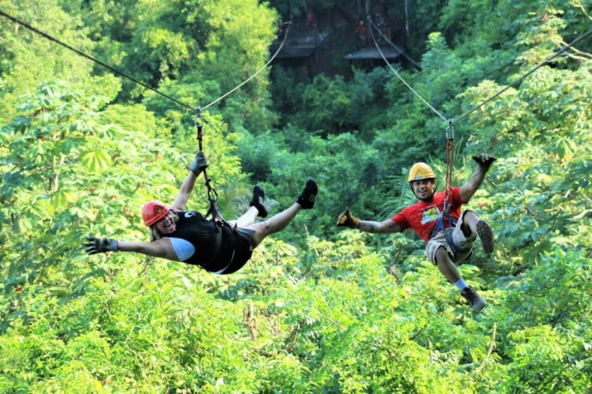 two persons hanging along a zip line while surrounded by greenery