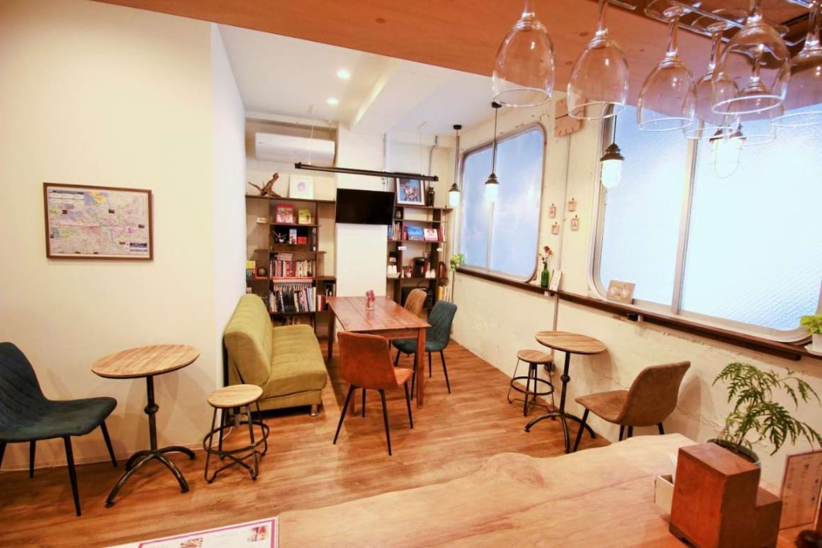 A cozy communal space with wooden tables, colorful chairs and large glass windows in Hostel TOKI