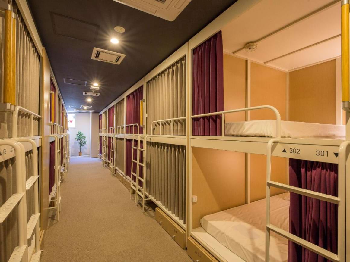 Two-level capsule rooms with yellow lighting and curtains down a hallway in Hotel Hostel SAPPORO