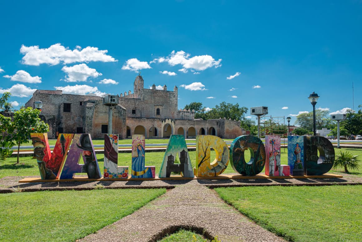 A large, colorful sign that reads "Valladolid" in front of an stone building.