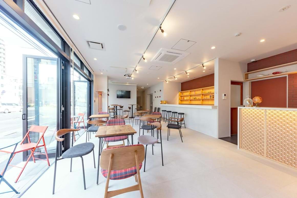 A large, open communal space filled with tables and chairs in plat hostel keikyu sapporo ichiba