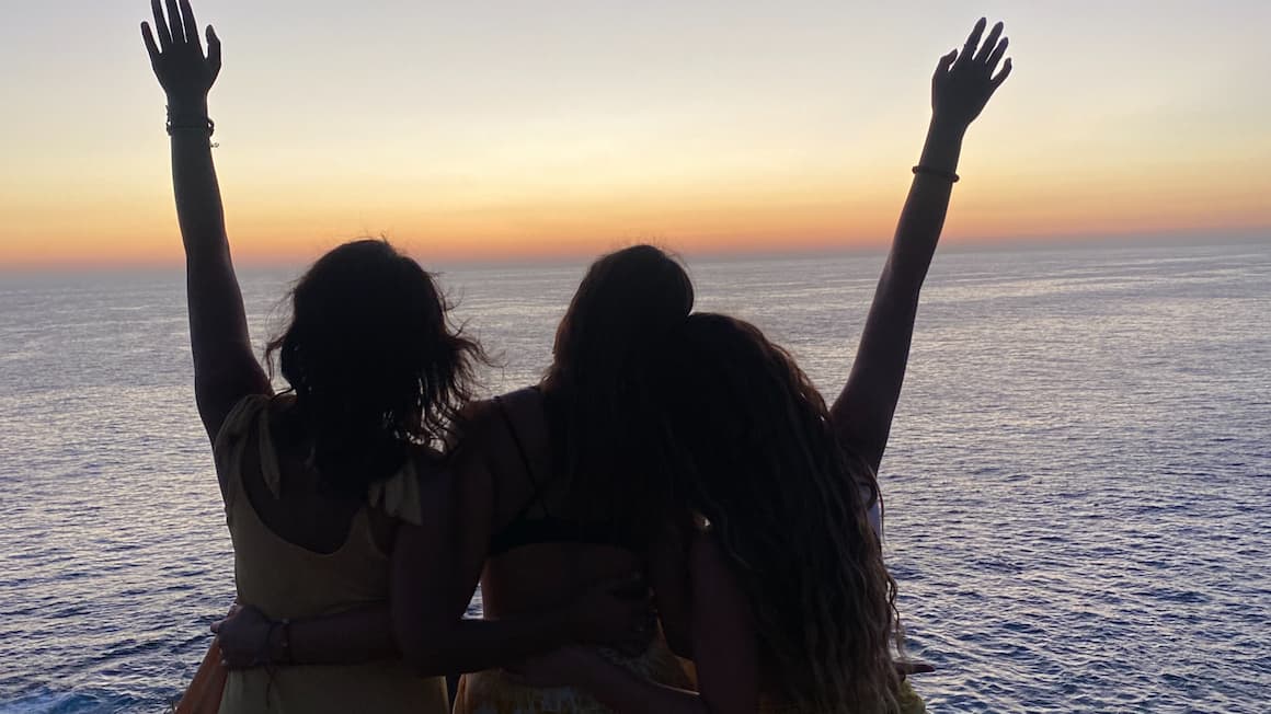 three friends looking at the ocean as the sun sets