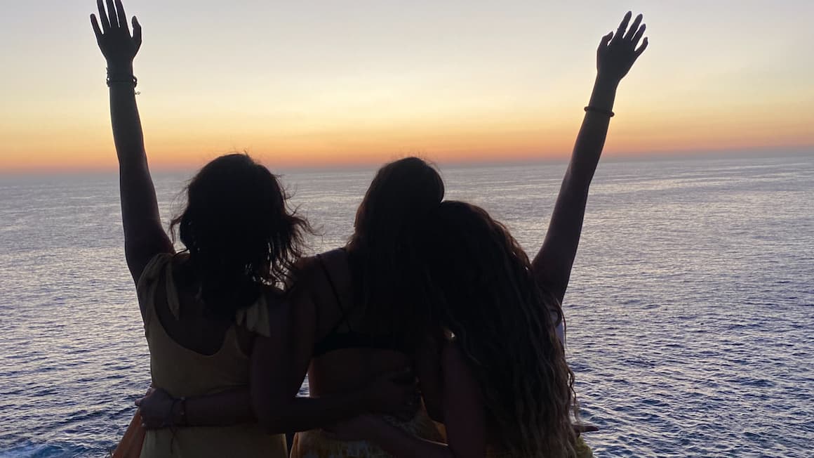 three friends looking at the ocean as the sun sets 