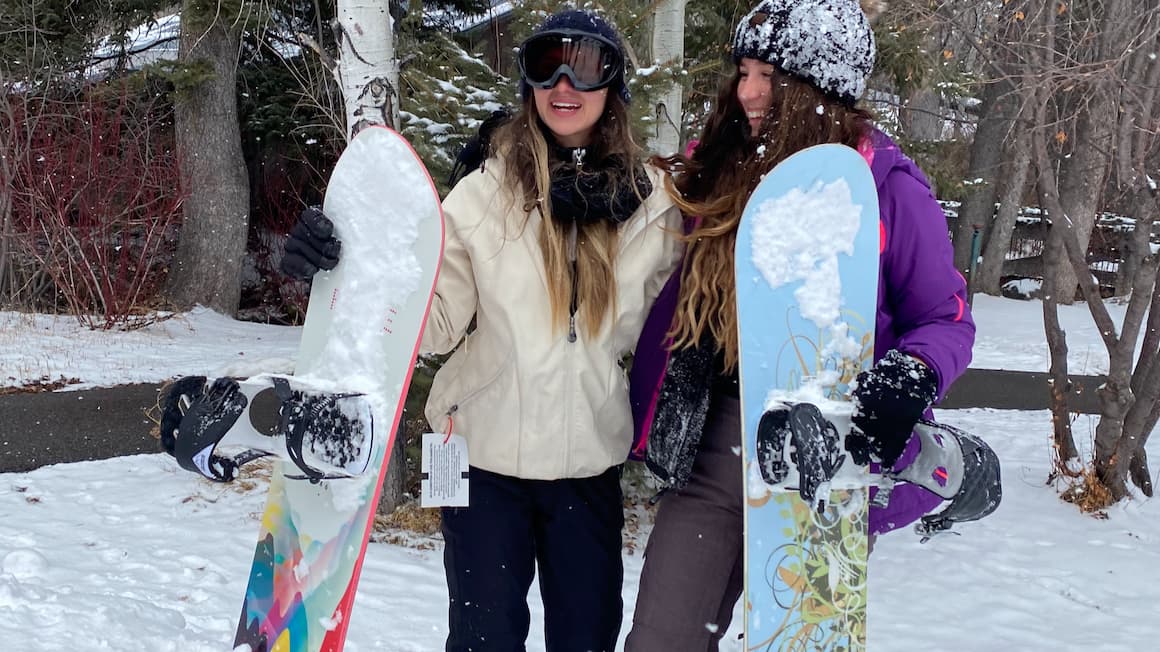 two girls smiling holding snowboards on a snowy mountain 