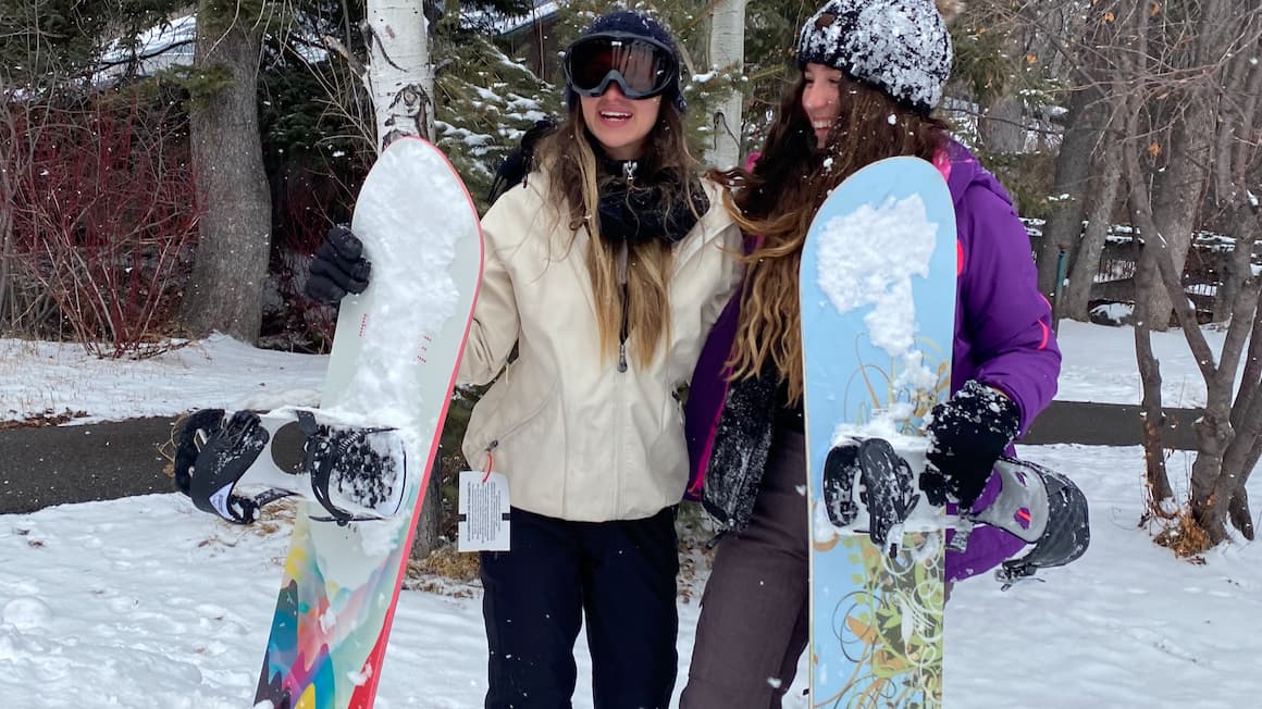 two girls smiling holding snowboards on a snowy mountain