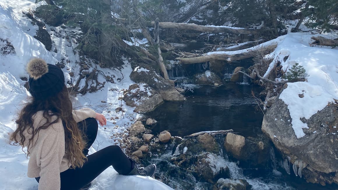A girl sitting next to the river as it snows in the mountains of Utah, usa  