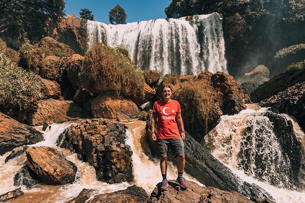 A person standing in front of a large waterfall on a rock in the centre in Vietnam