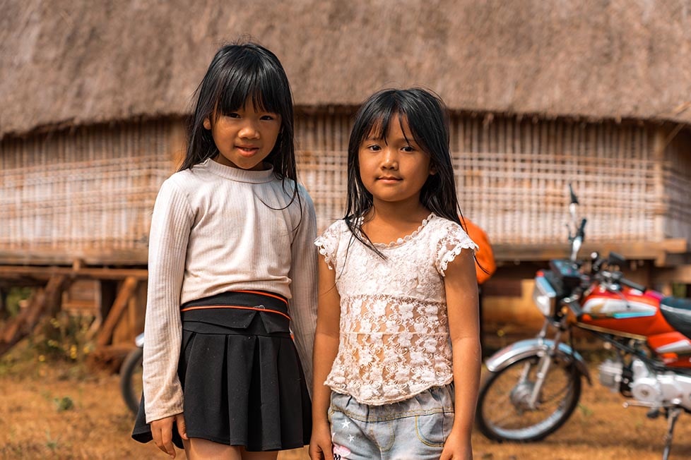 Two young girls standing in front of a tribal house in a village in remote Vietnam