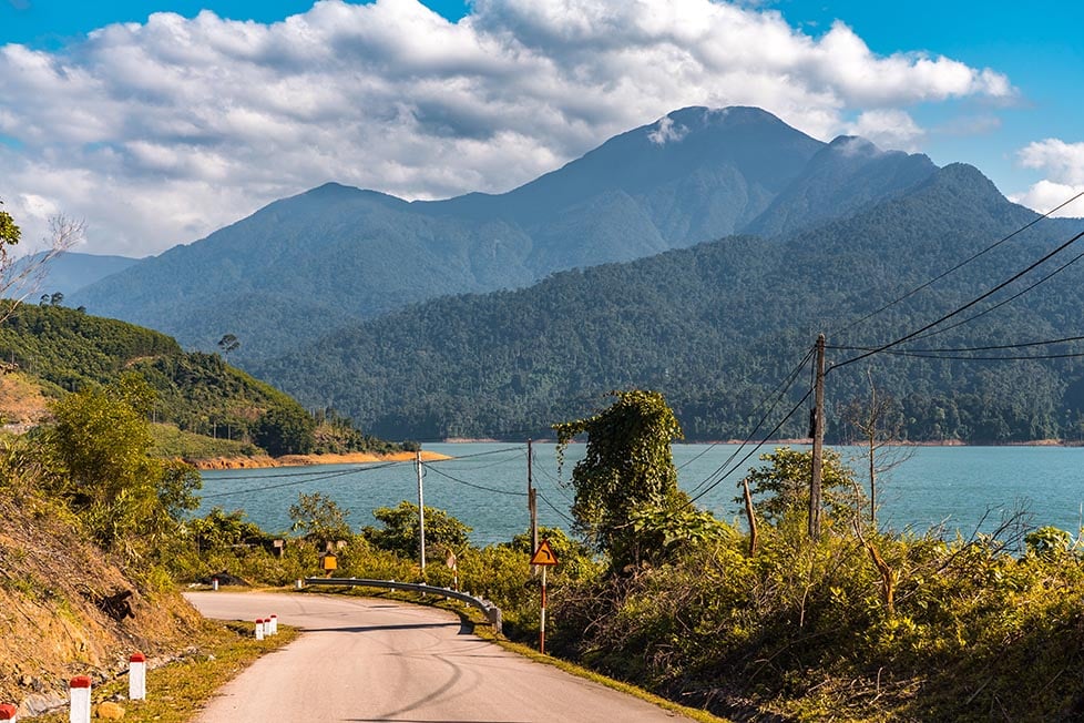 A blue lake with a road running alongside it and mountains in the distance in Vietnam
