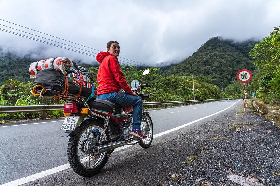 A person on a motorbike/ motorcycle with a backpack on their bike and mountains in the background