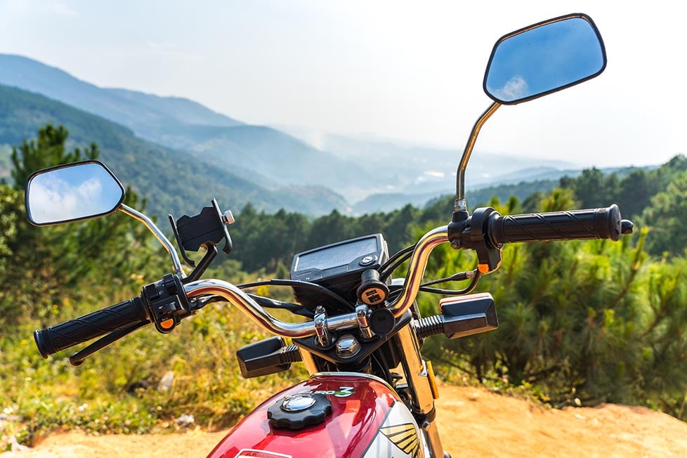 A motorbike/ motorcycle in the foreground with rolling mountainside in the distance