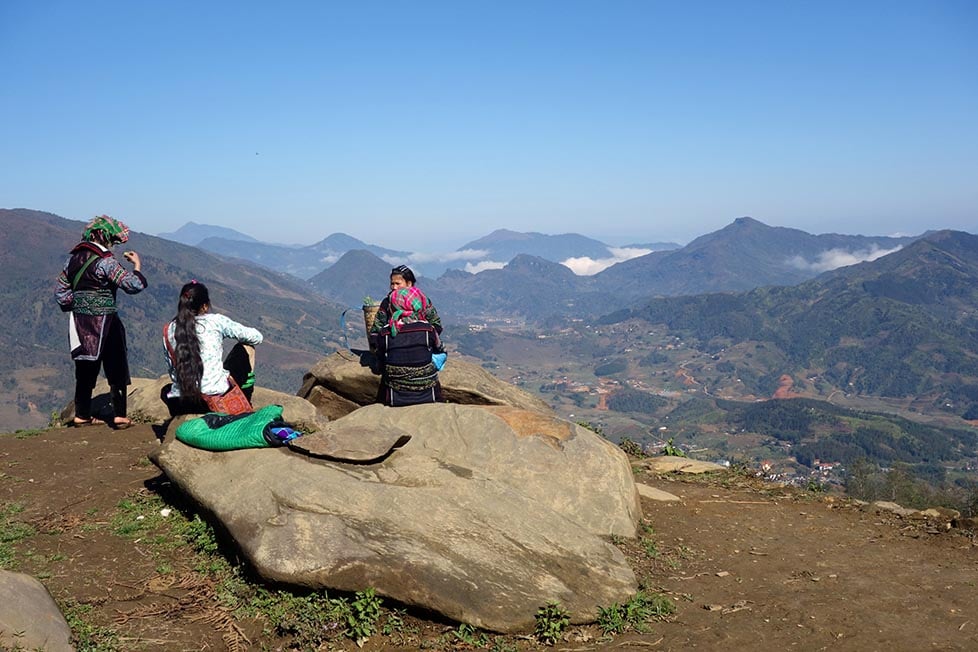 Four tribal women in traditional clothing sitting overlooking the mountains and rice paddies of Sapa, Vietnam