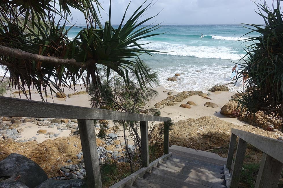 Steps looking down on the the beach with a person surfing in the distance in Byron Bay, Queensland, Australia