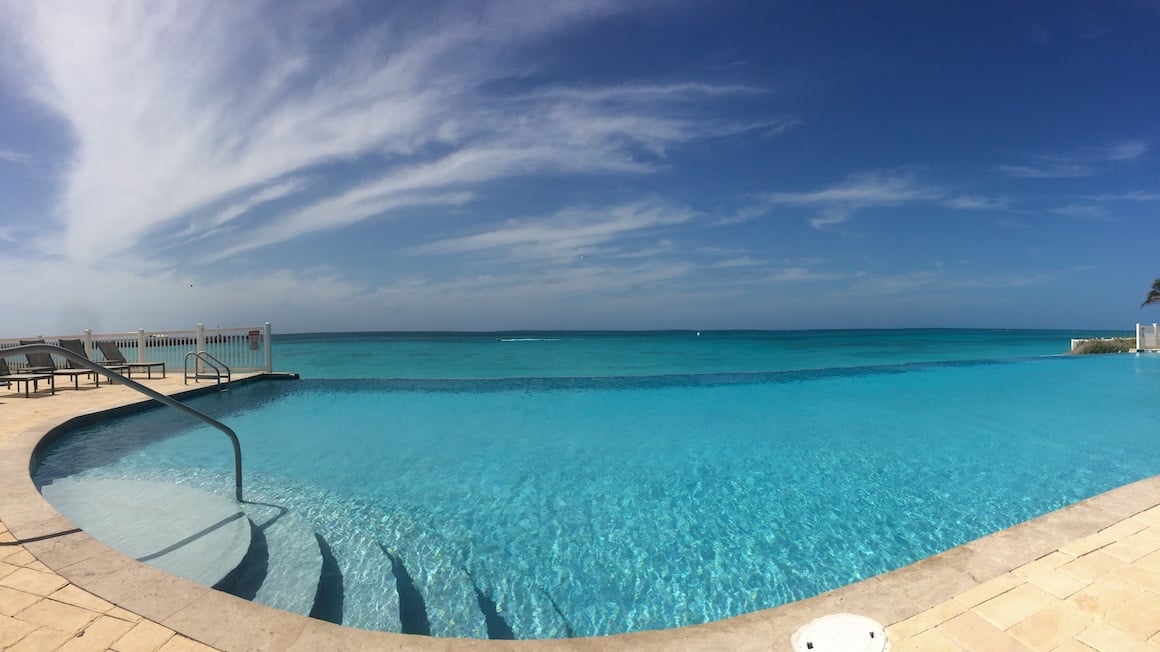 a bright blue infinity pool seen on a sunny cloudless day that looks like it's attached to the ocean in the bahamas