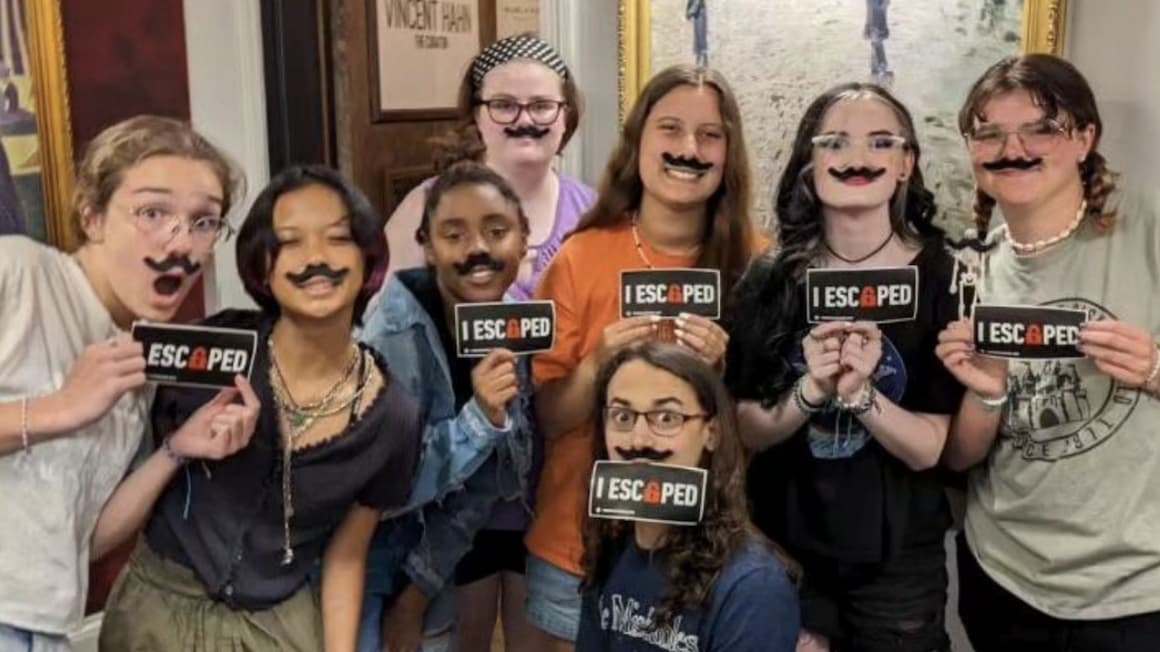 a group of teenagers smiling for a picture with fake mustaches on at an escape room