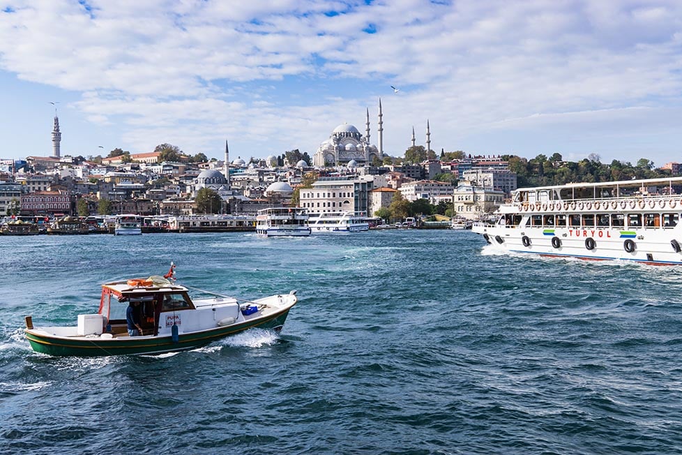 A boat crossing the Bosphorus with a large mosque and several other minarets from smaller mosques in the distance.