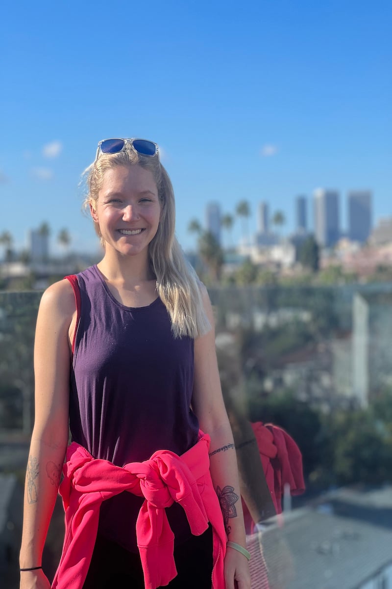 girl standing on a hotel roof top with palm trees and skyscrapers in the background in los angeles california