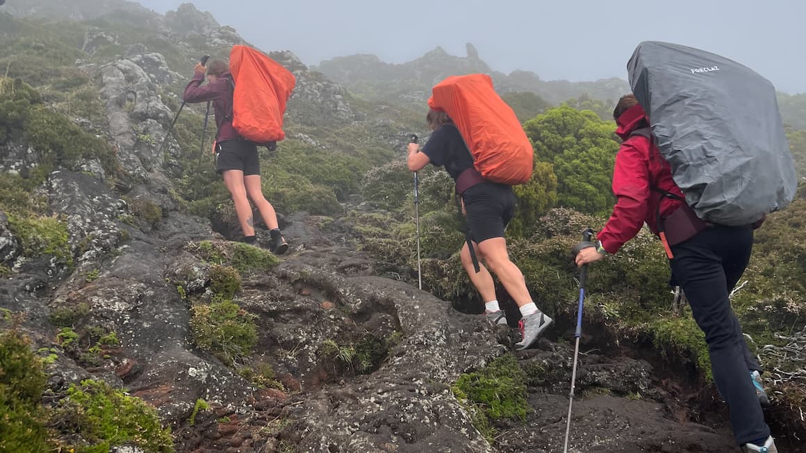 three friends hiking up a mountain with backpacks on and using hiking poles for guidance