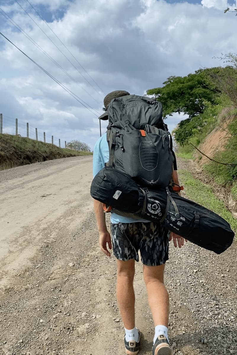 a guy with his backpack on as he hitchhikes in costa rica