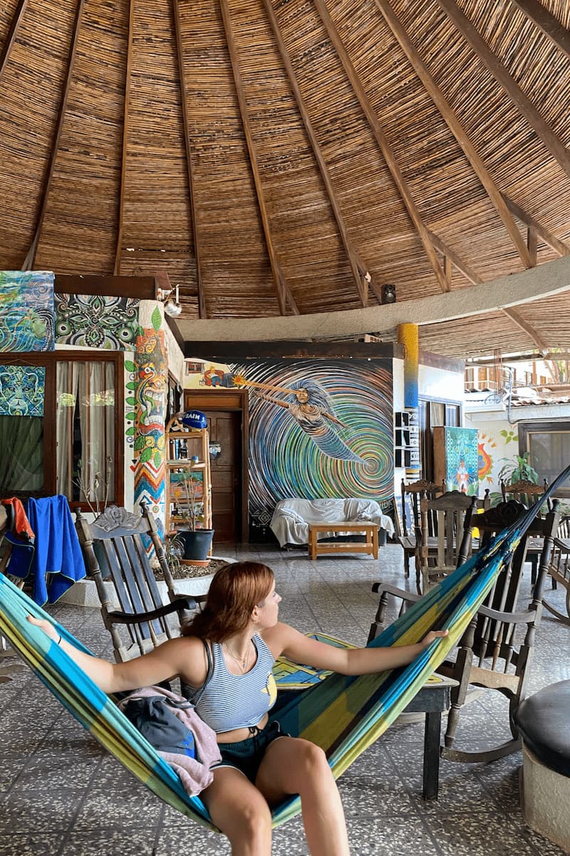 a girl sitting in a hammock in the common area of a hostel in costa rica