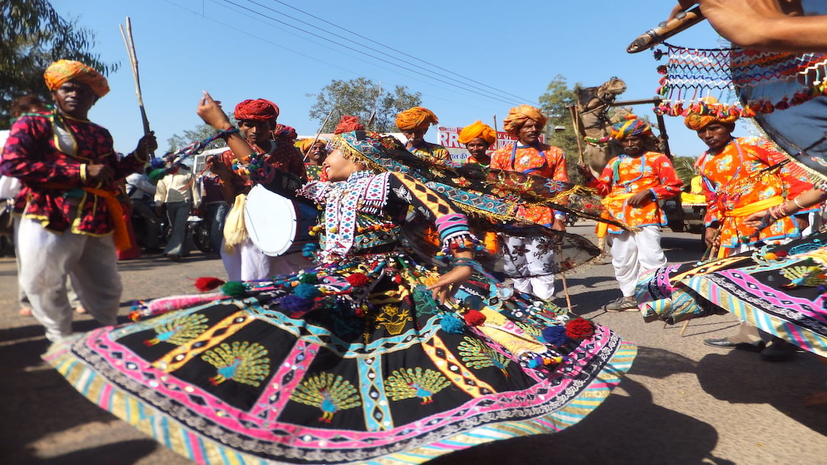 girl wearing a multicolored dress dancing in the street with men playing instruments in india