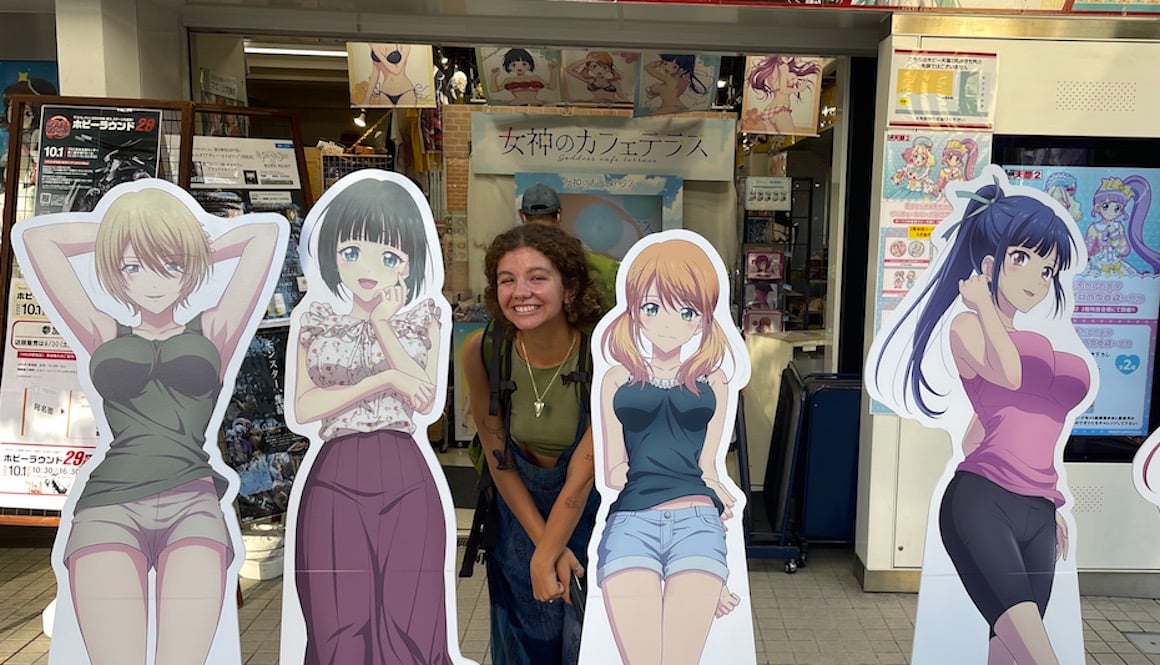 A girl stands amongst cardboard cutouts of anime characters in Kyoto, Japan.