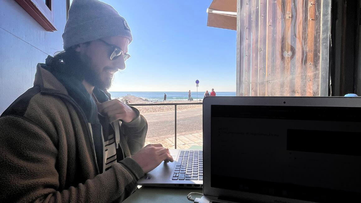 man smiles while remote working at a beach near lisbon, portugal