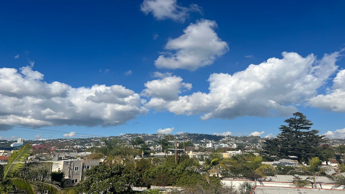 a sunny day with blue sky and fluffy crowds over the green hilly neighborhood of beverly hills in los angeles california usa