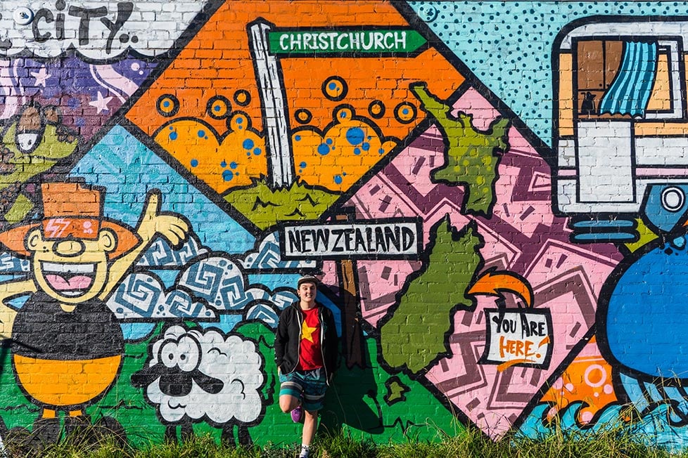 A person stood by a wall with graffiti showing different imagery related to New Zealand in Christchurch, New Zealand