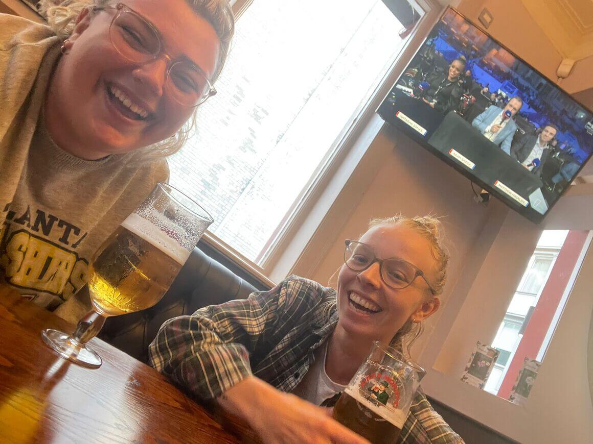 two women laughing with two pints of beer on the table.