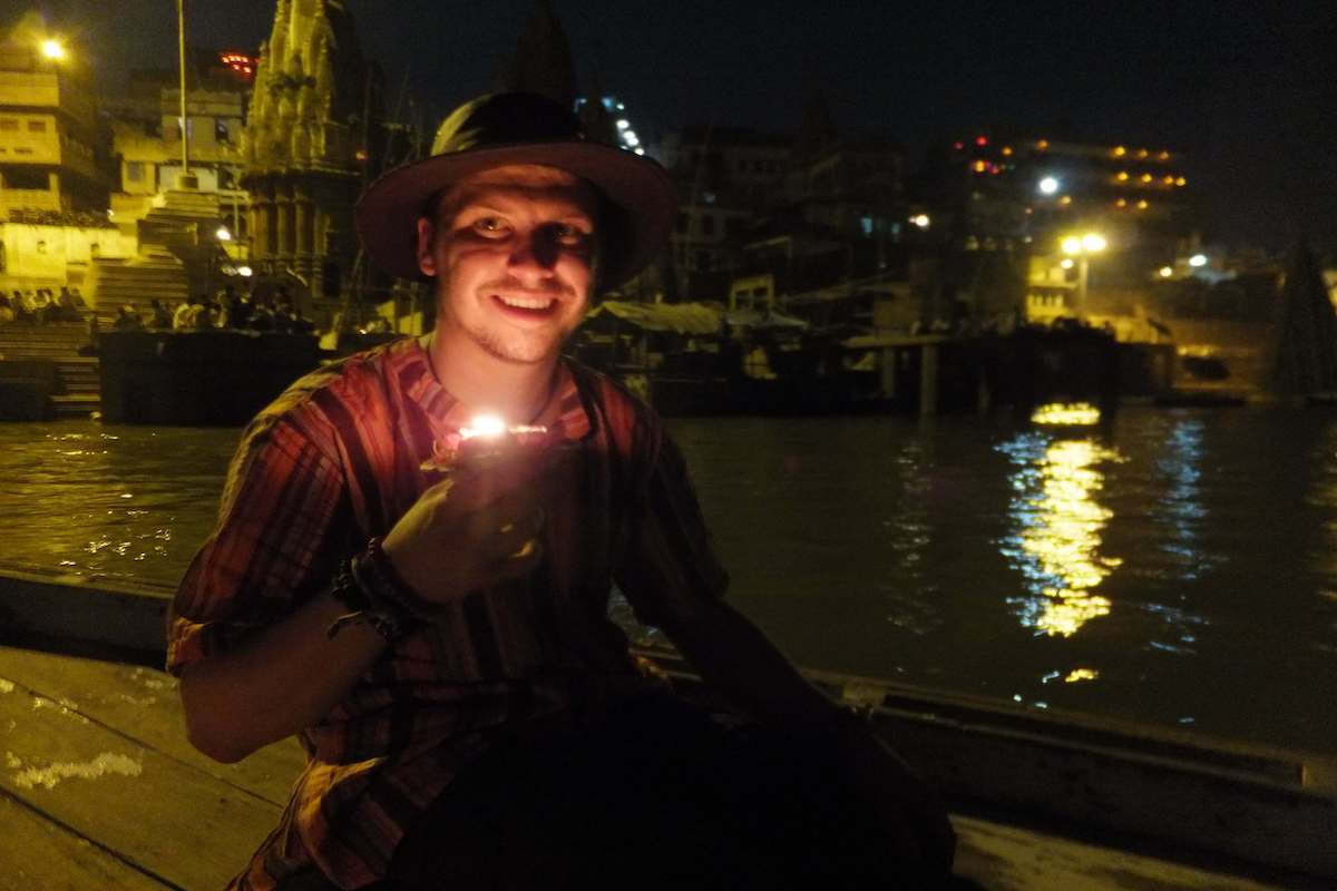 a man sitting pon a boat at night in varanasi india holding a candle offering