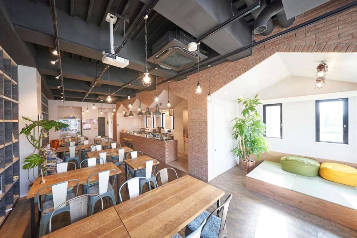 co-working space with wooden tables, colorful chairs and a small seating area in WeBase Hakata Hostel