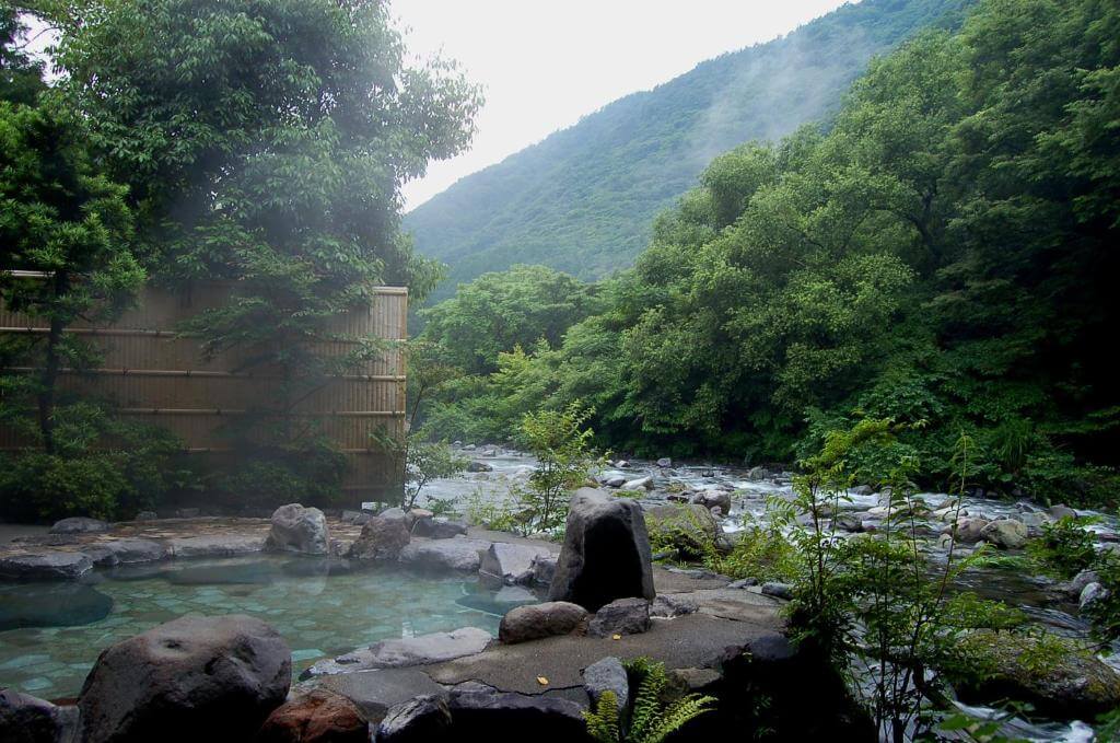 stone hot tub filled with hot water surrounded by lush greenery and spring at Kijitei Hoeiso