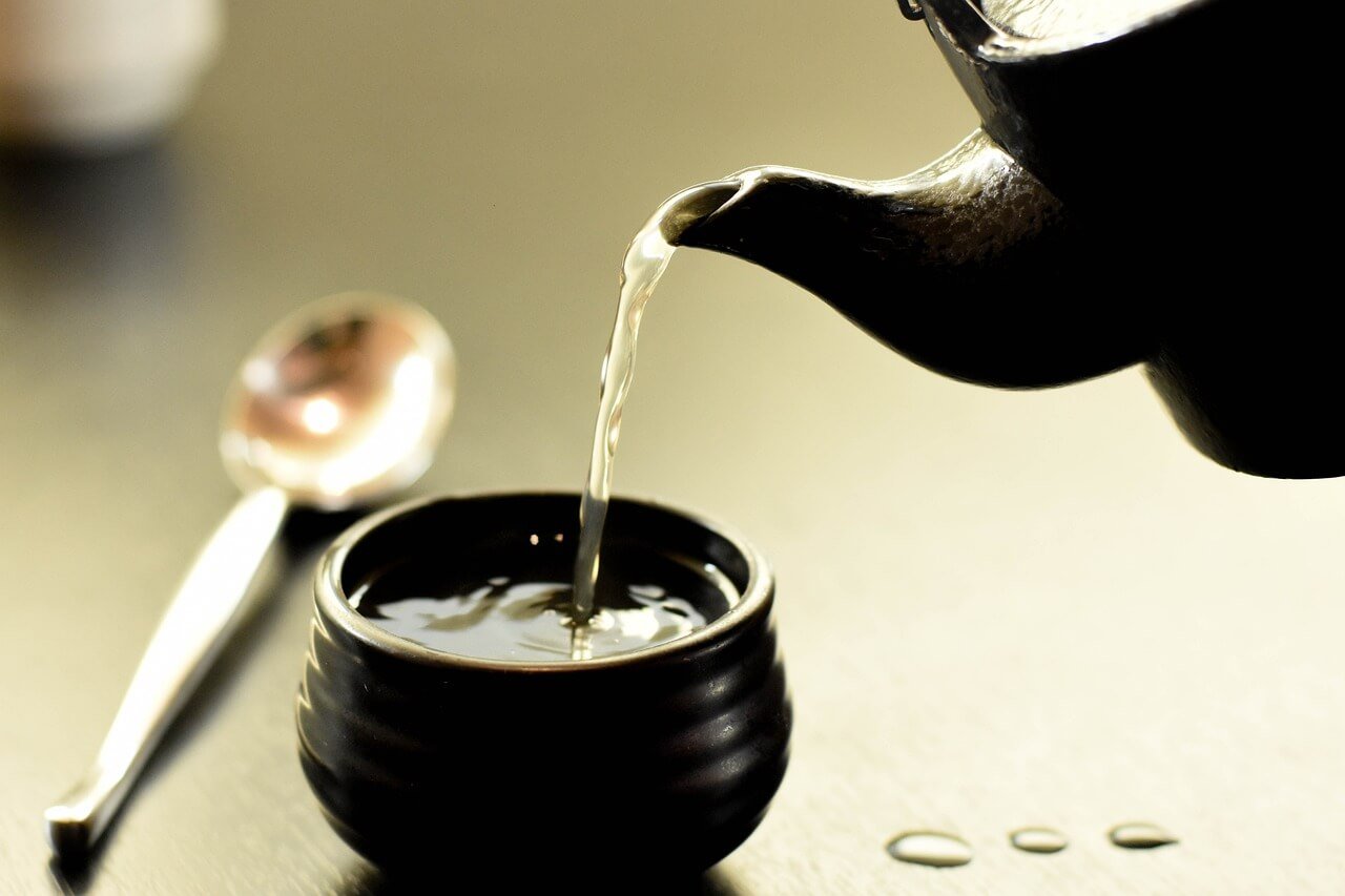 Steaming kettle pouring freshly brewed tea into a cup