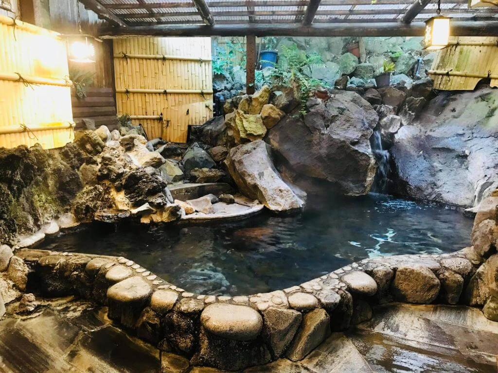 A stone hot tub filled with clear water sits nestled among rocks.