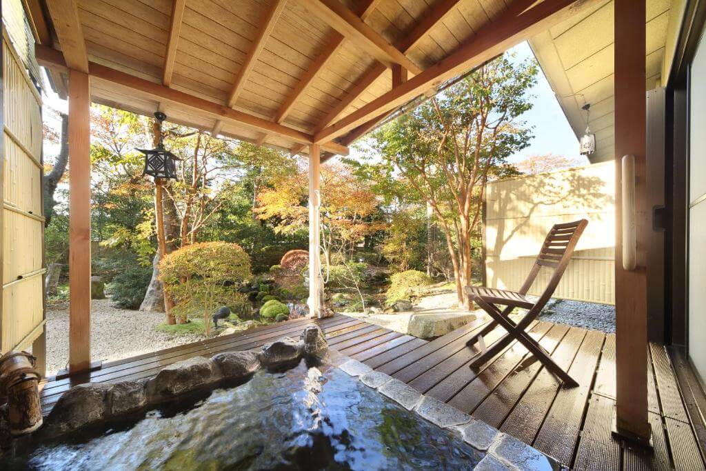 a wooden deck with a hot tub full of water surrounded by a lush garden at Yoshimatsu, Hakone
