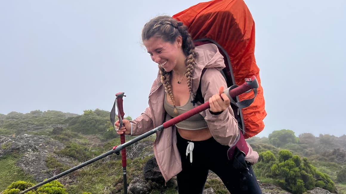 A girl trekking a mountain with a backpack on and trekking poles in her hands