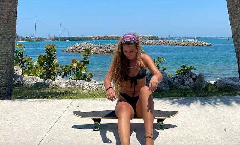 a girl sitting on a skateboard with the beach and palm trees behind her in ,Miami, Florida, USA